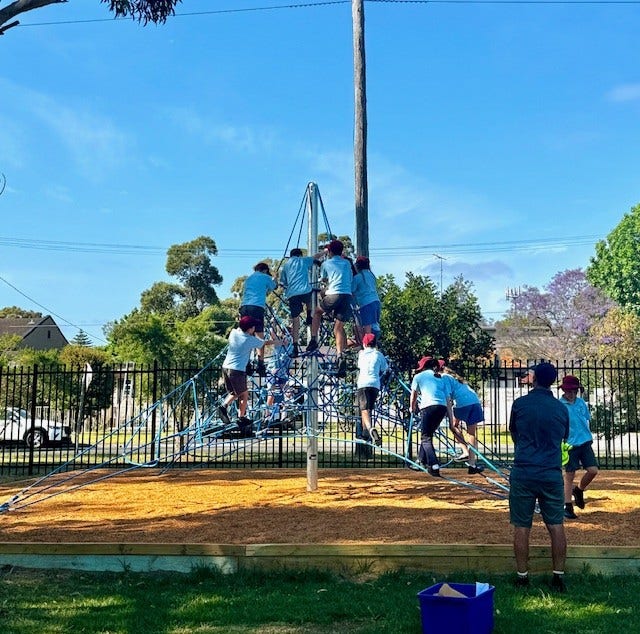 kids playing on the skyclimber in the playground with a teacher supervising