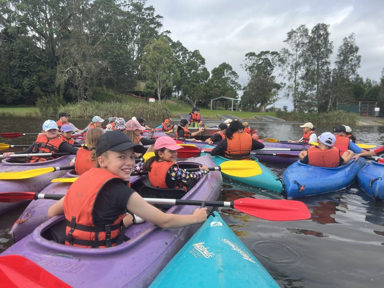 a bunch of very colourful canoes on the river with kids in them in a big group waiting to go down the river