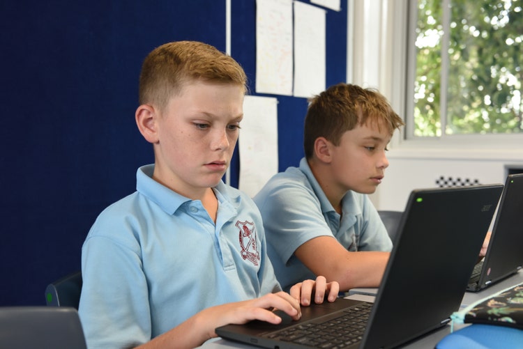 Two boys sitting at a desk working on laptops