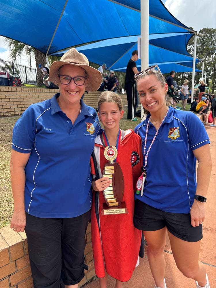 two teachers with a student that is holding a perpetual zone swimming trophey beside the competition pool